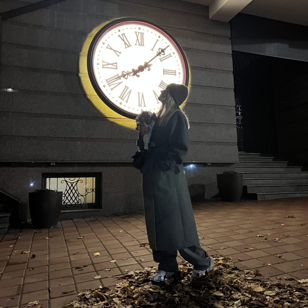 Співачка Kola, великий годинник, жіноче сіре пальто, осіннє листя