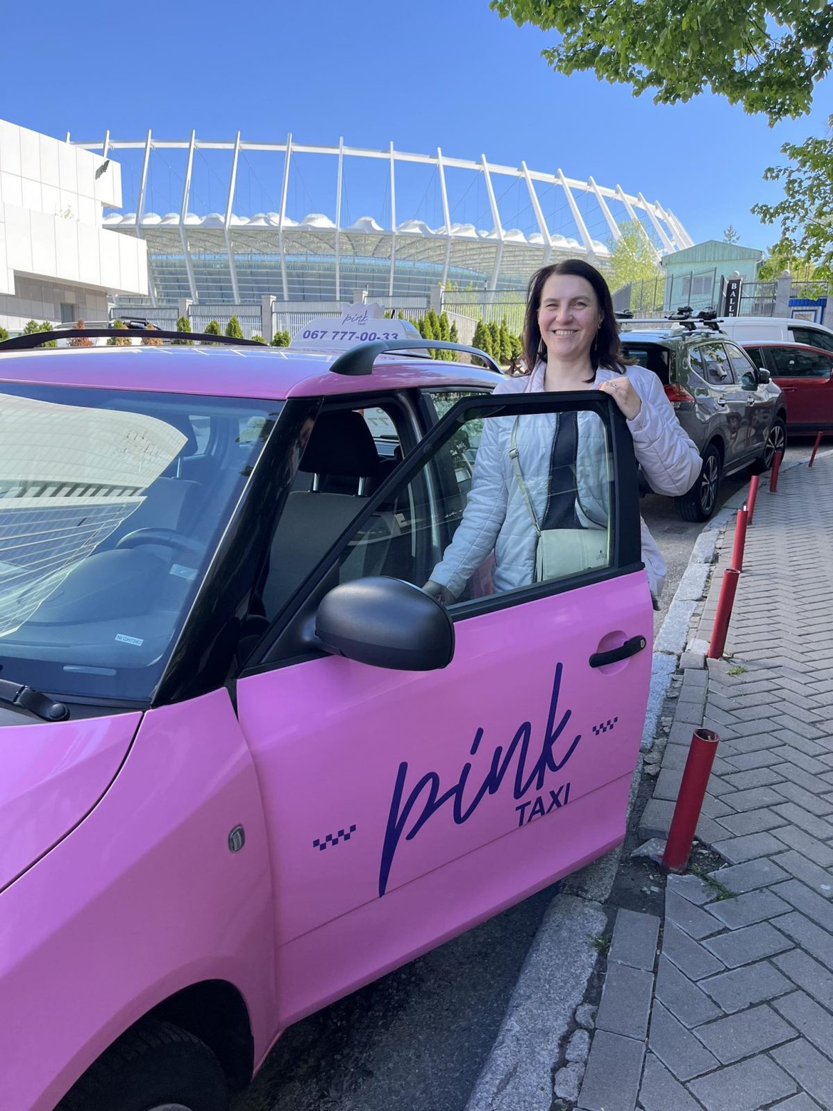 Водійка Олена стоїть біля відкритих дверцят машини Pink Taxi 