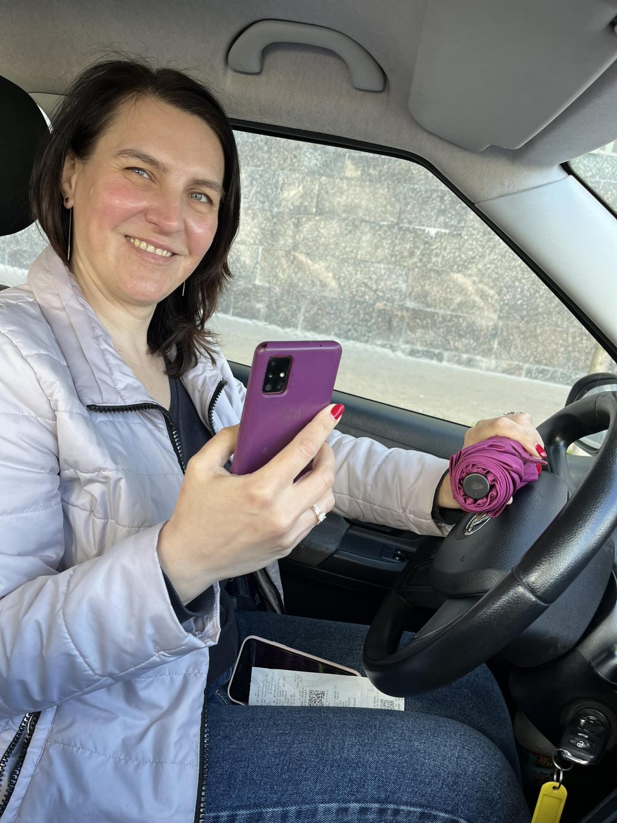 Водійка Олена з телефоном та парасолькою сидить в машині Pink Taxi 