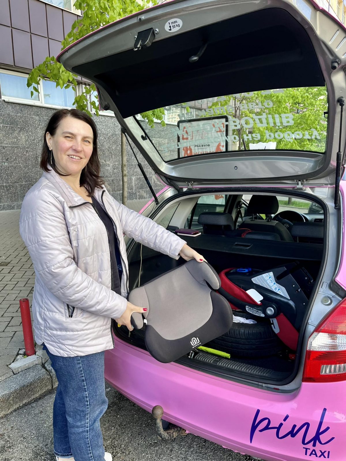 Водійка Олена демонструє автокрісло біля машини Pink Taxi 